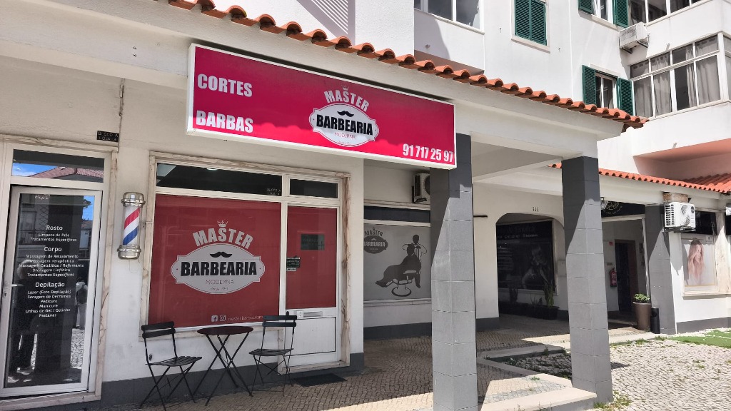Fachada da Master Barbearia em Cascais com letreiro oficial vermelho, poste de barbeiro clássico e duas cadeiras à entrada.
